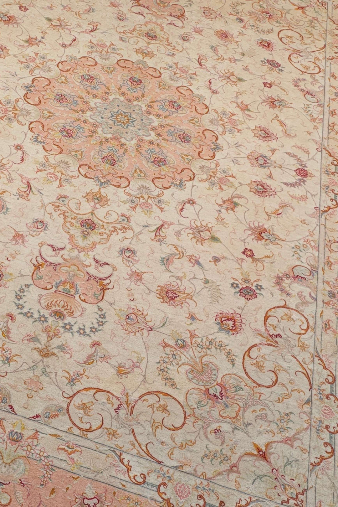 Scrolling leaf medallion detail in ivory and peach on Tabriz rug